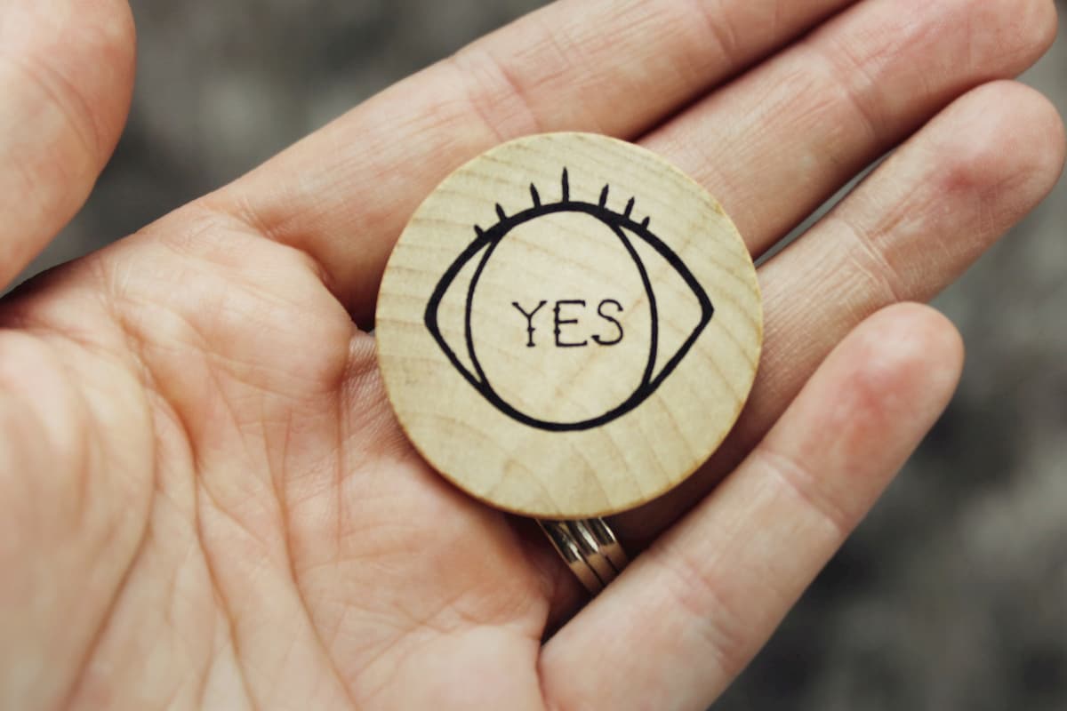 A hand holding a wooden disc that had an eye with the word yes drawn on it